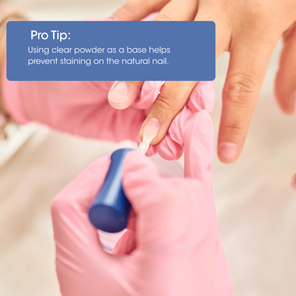A pro tip for dip manicures: Using clear powder as a base helps prevent staining on the natural nail. A nail technician is shown applying a product to a client's nail.