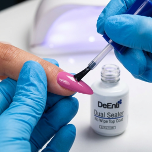 Professional nail tech wearing blue gloves applying DeEnti Dual Sealer no wipe top coat over pink acrylic nail enhancements.