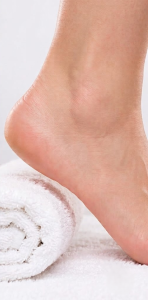 Close-up profile view of a smooth, healthy, callus-free female foot and heel resting flawlessly in a clean, high-key setting on a plush rolled white towel. The skin is immaculate, showing the effective result of callus removal.