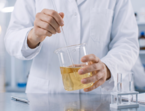 Close-up of a cosmetic chemist stirring a yellow liquid formulation in a glass beaker during domestic product development.